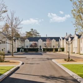 A picturesque, rustic manor lodge surrounded by lush greenery and a red brick pathway, under a clear blue sky, conveying tranquility and charm of countryside life.