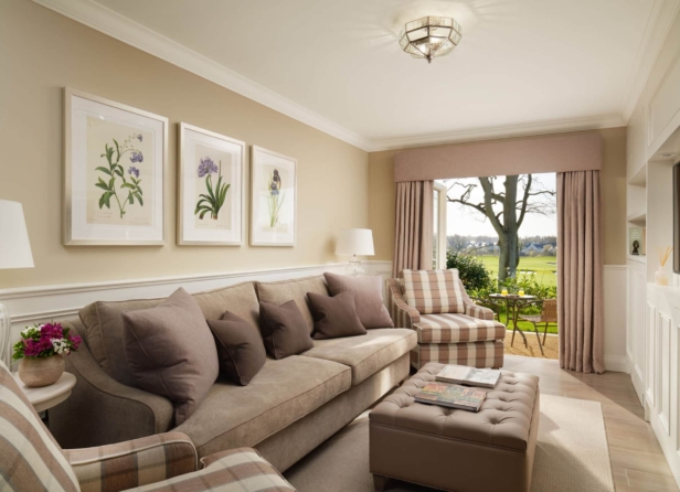 A cozy sitting room with elegant furnishings, featuring a piano, plush sofas, a coffee table, and large windows covered by sheer drapes, creating a warm and inviting atmosphere.