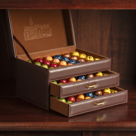 A box of assorted signature bonbons, arranged neatly in rows, showcasing various vibrant colors and decorative patterns on each chocolate piece.