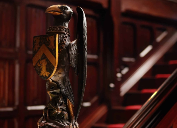 Image of Adare Manor surrounded by lush greenery and trees, with a clear blue sky and a raven gracefully flying above.