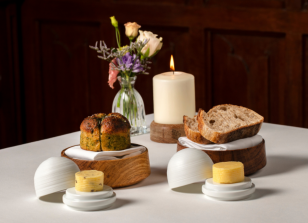 A loaf of rustic whole-grain bread with a crispy, golden-brown crust, displayed on a wooden cutting board, surrounded by flour and wheat stalks for a rustic look.